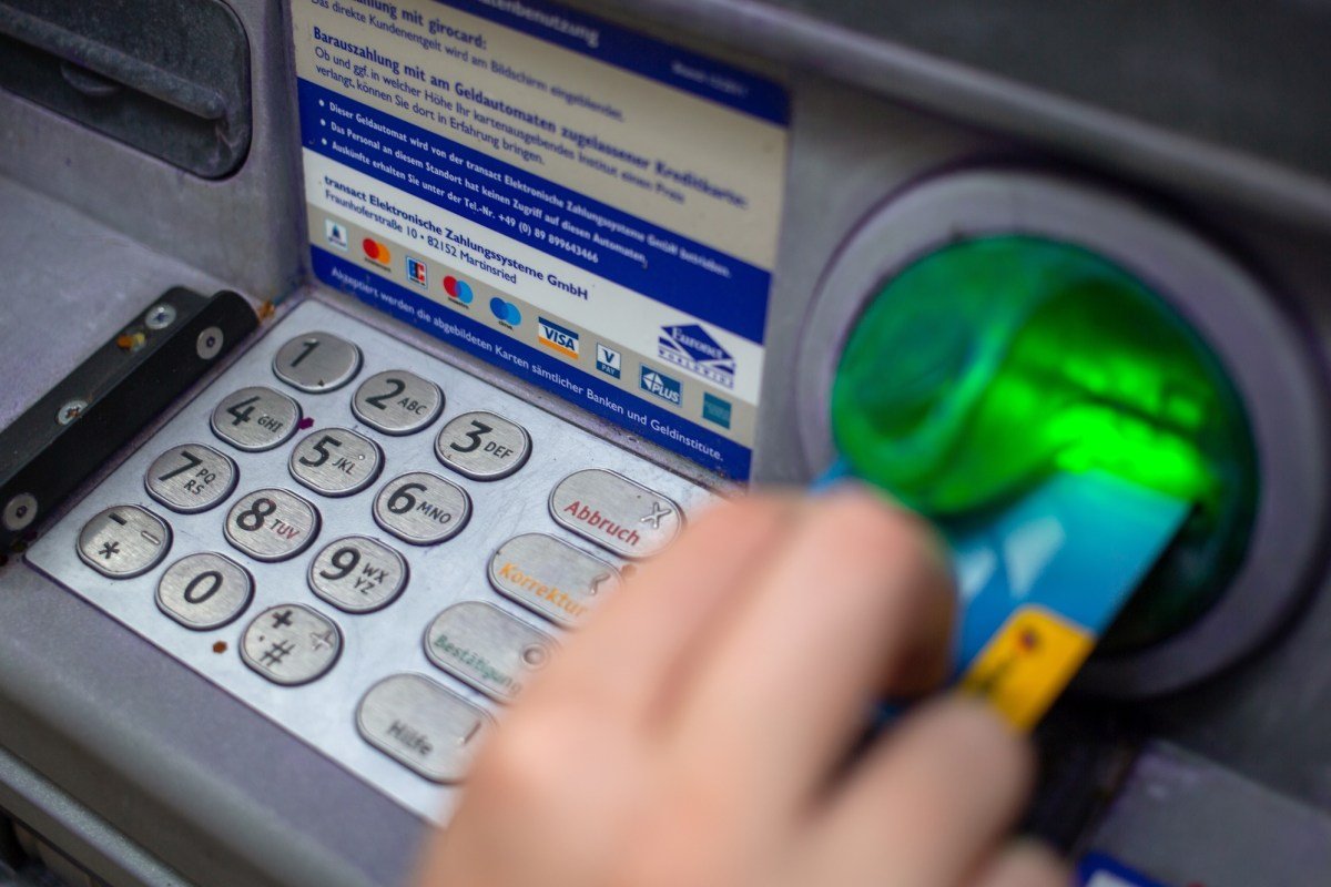 a close-up photo of a person punching in their PIN on an ATM in a wall.