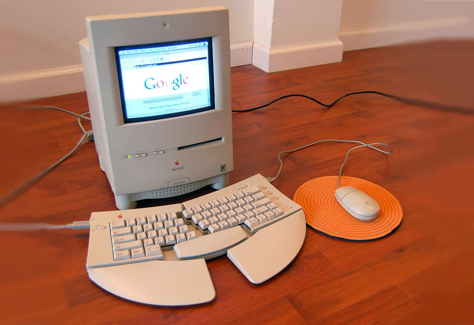 Photograph of a Macintosh Color Classic with split keyboard and mouse, sitting on a hardwood floor